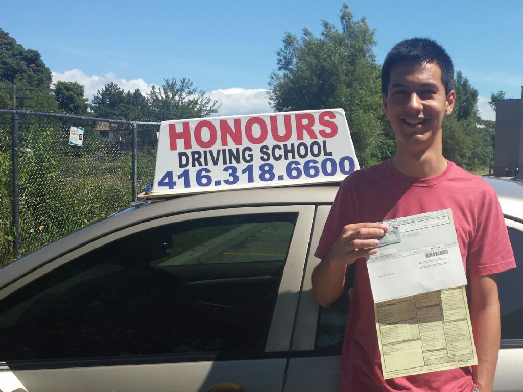 Honours student holding a road test result beside the school car
